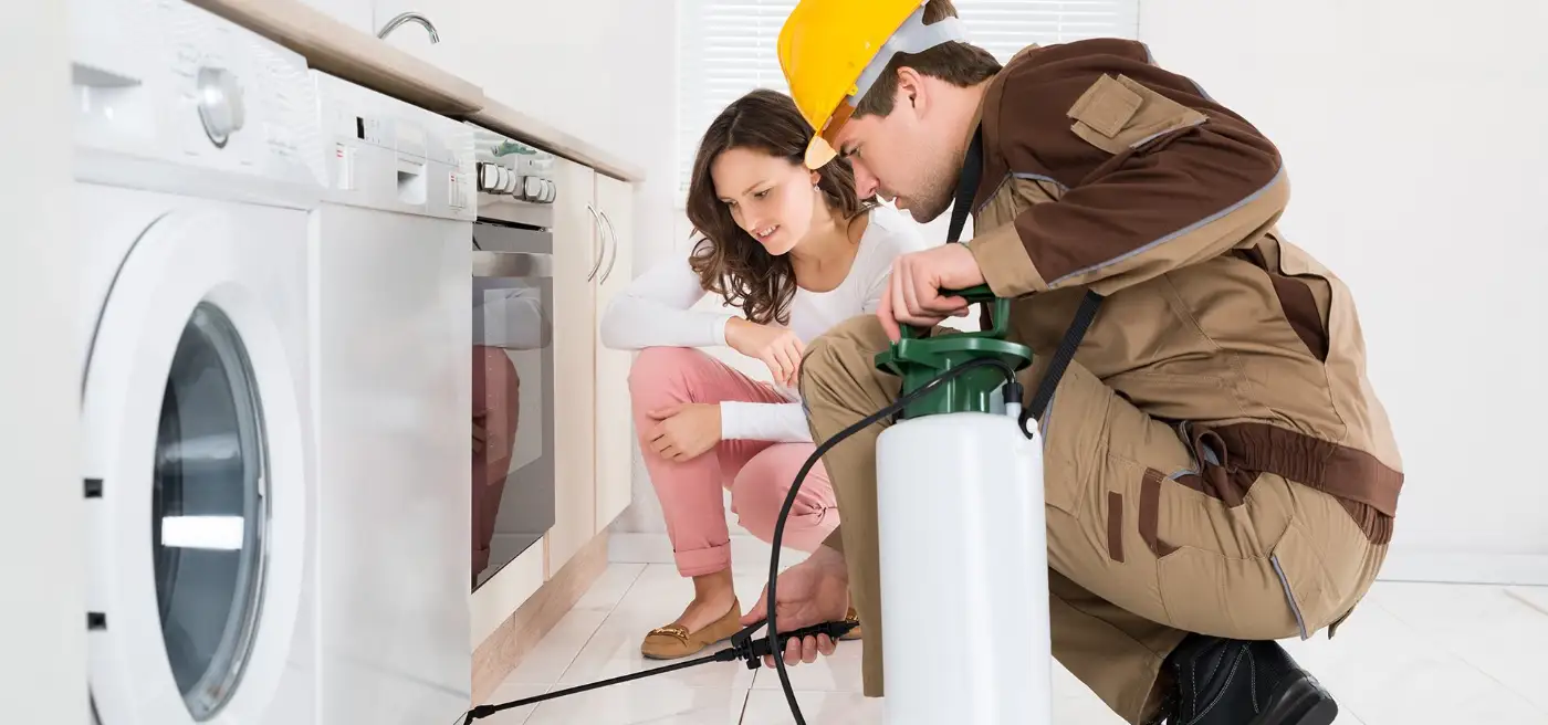 A pest technician treating along a kitchen floor while the homeowner watches